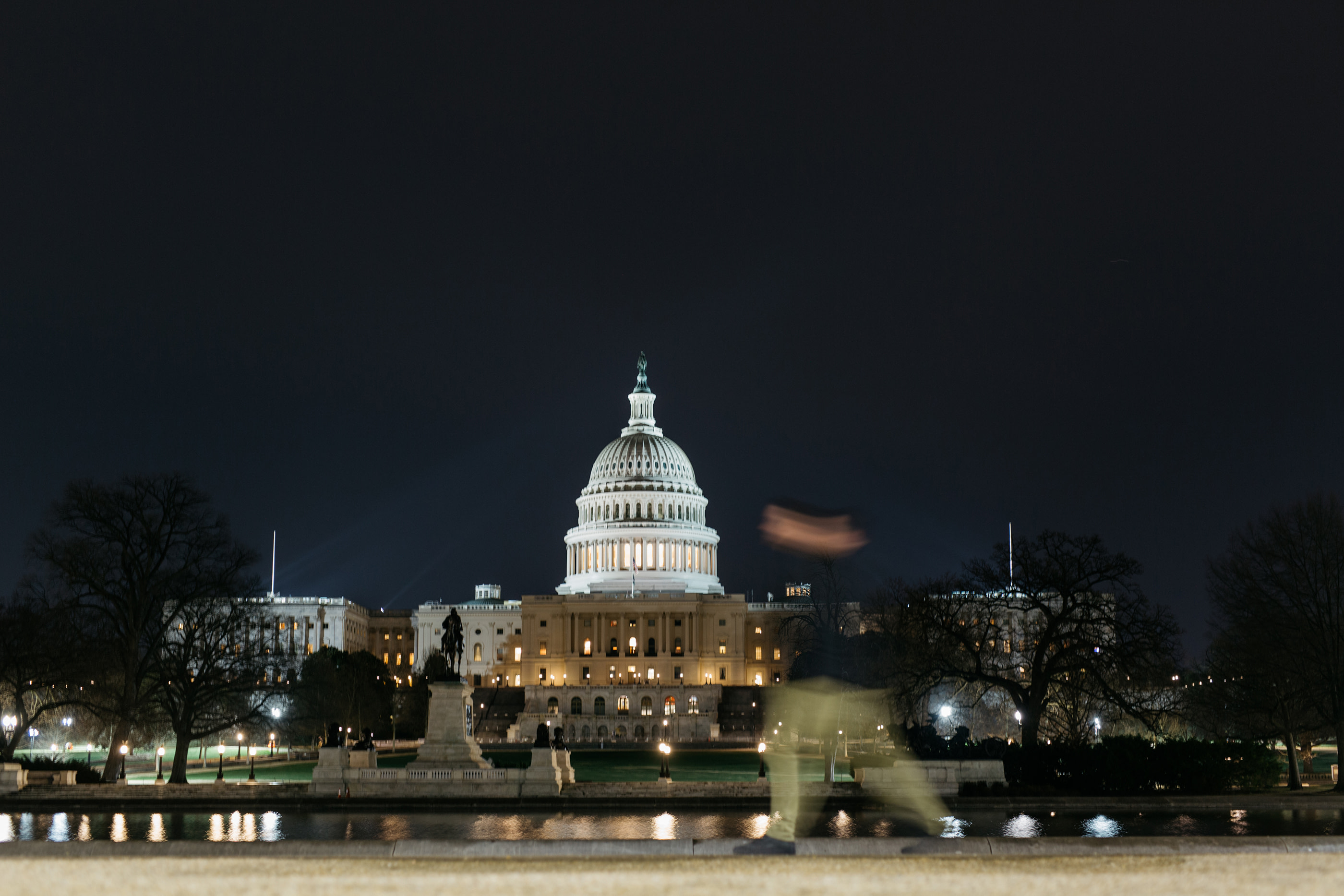 U.S. Capitol building at night with blurred pedestrian.