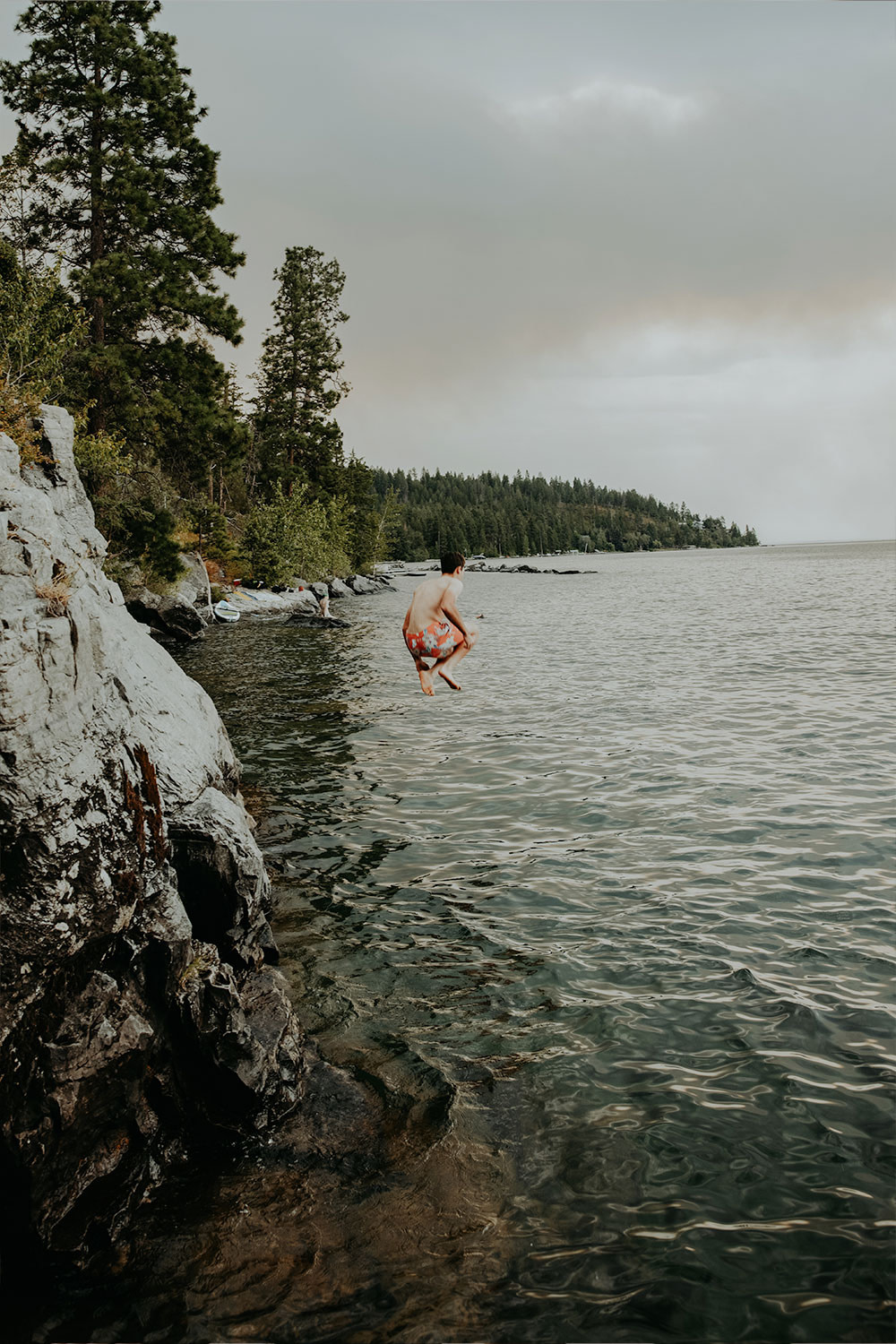 Young man in a swimsuit leaping from a cliff into a lake
