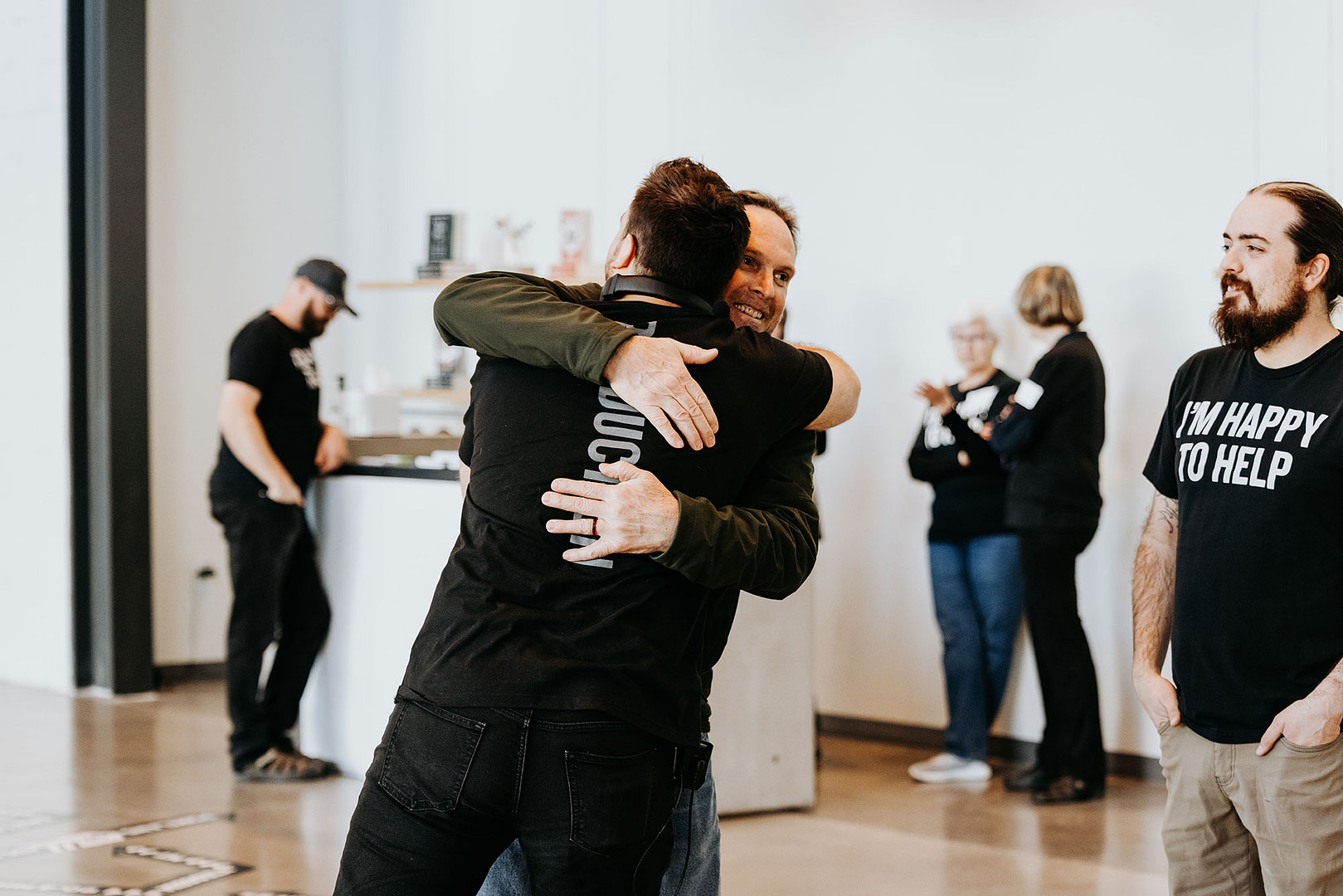 Two people hugging in large, modern looking room with wood floor and white walls