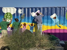 Volunteers painting colorful wall mural outdoors.