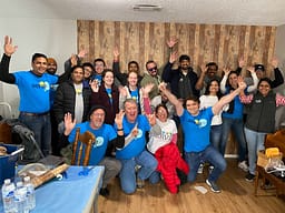 Group of smiling volunteers raising hands indoors.