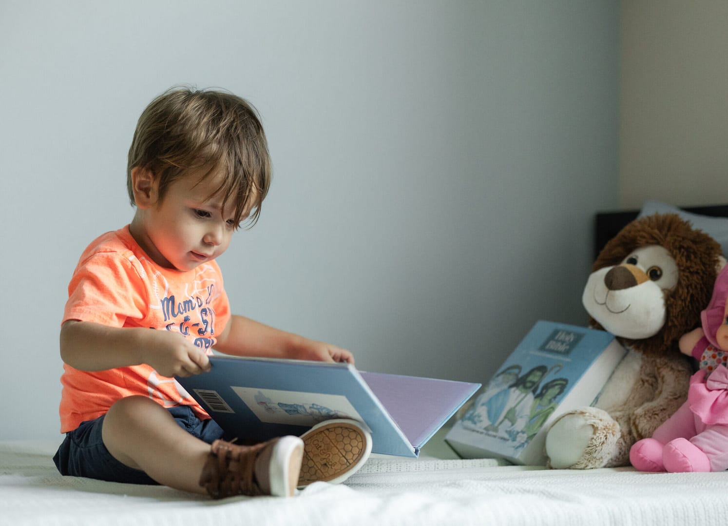 Child reading book on bed with stuffed toys.