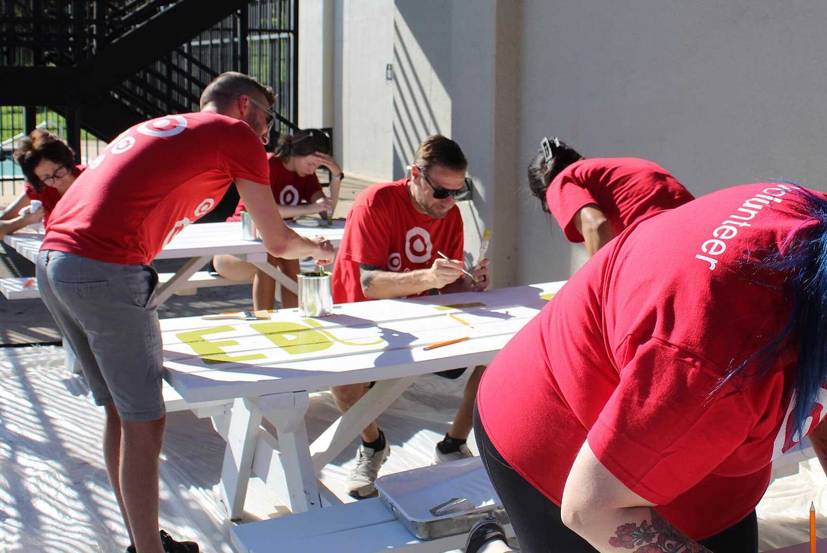 Volunteers painting outdoor tables in red shirts.