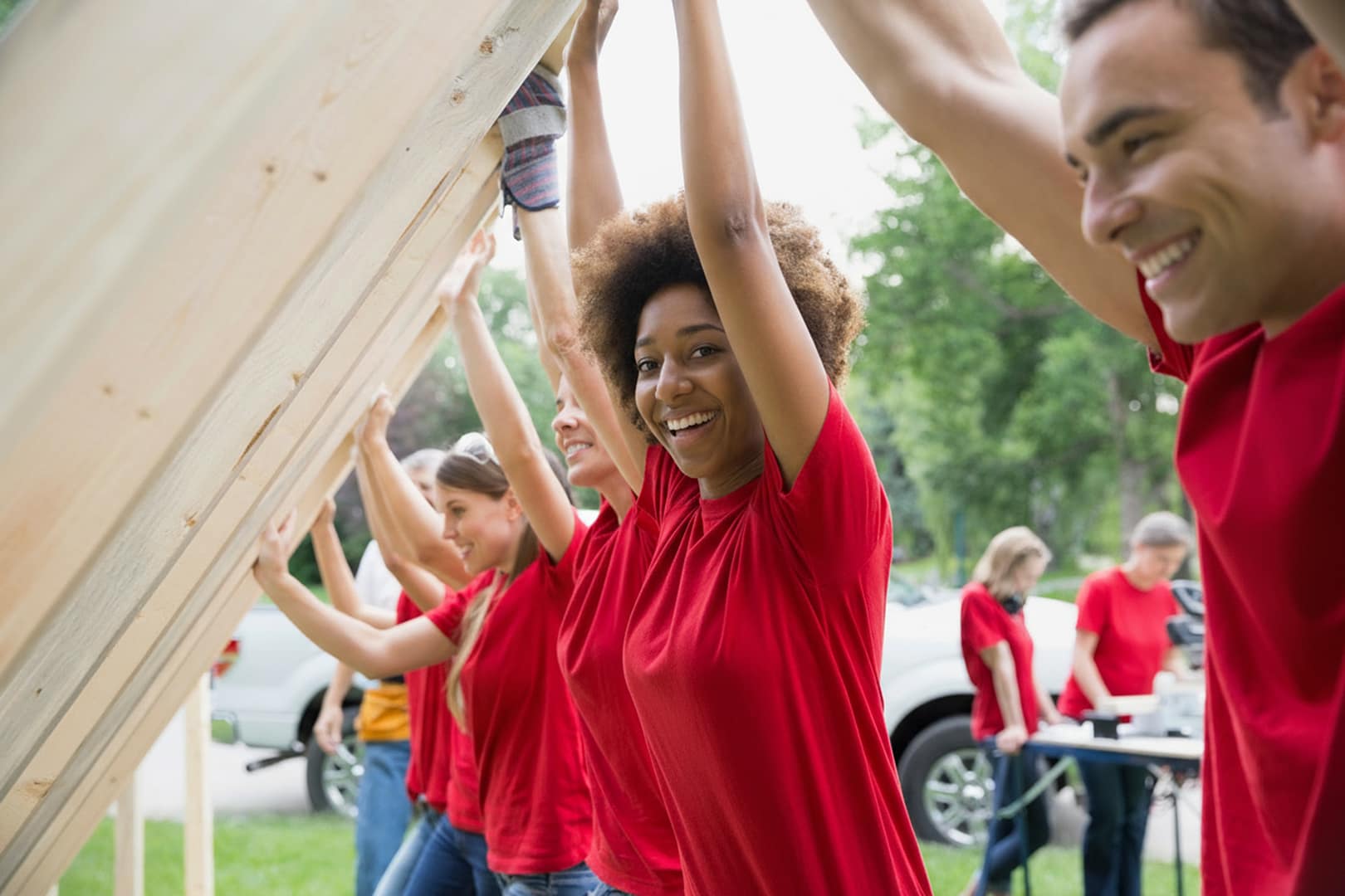 Volunteers lifting wooden structure outdoors, teamwork moment.