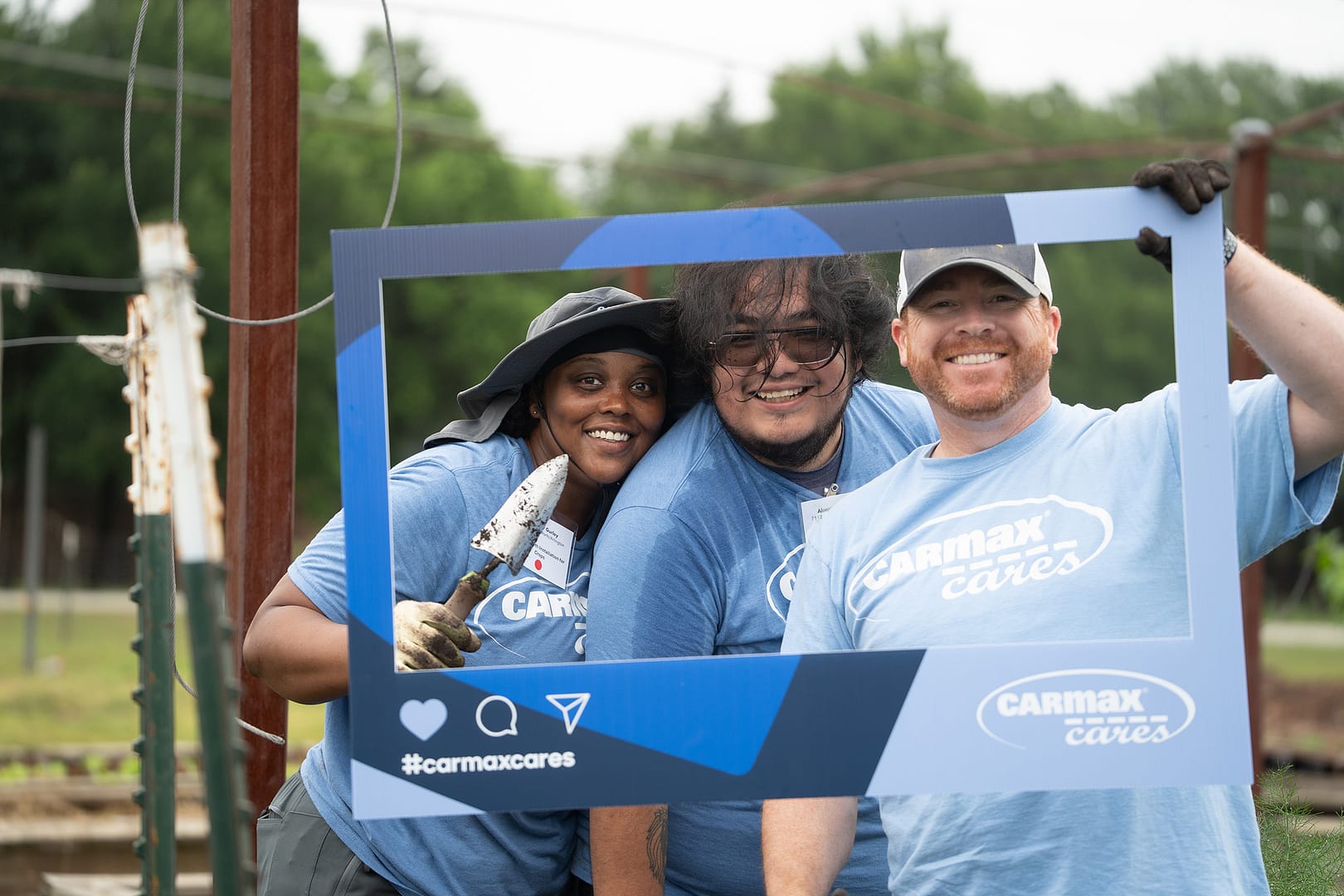 Three people smiling with CarMax Cares frame outdoors.