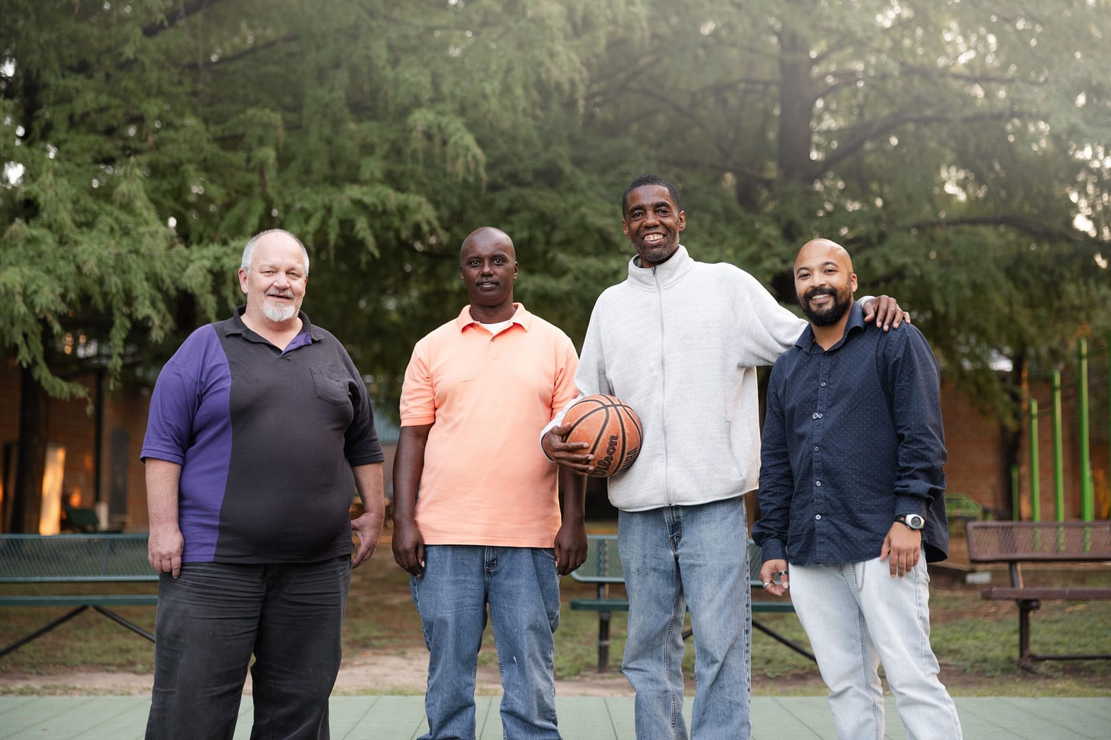 Four men smiling outdoors with basketball