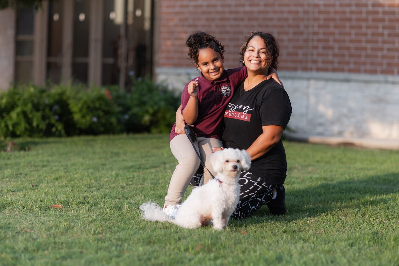Smiling woman and child with small white dog outdoors.