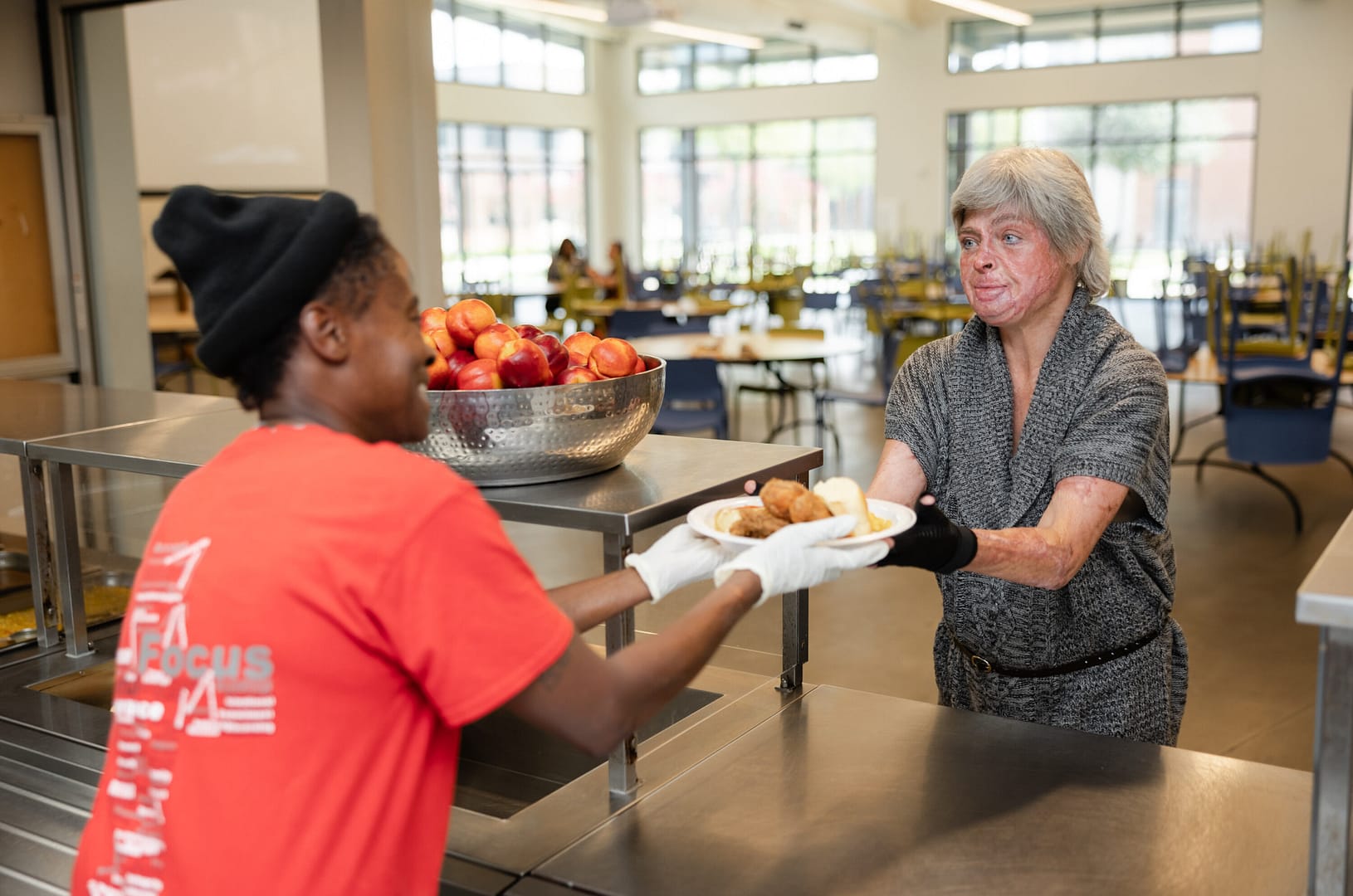 Cafeteria worker serving food to a customer.