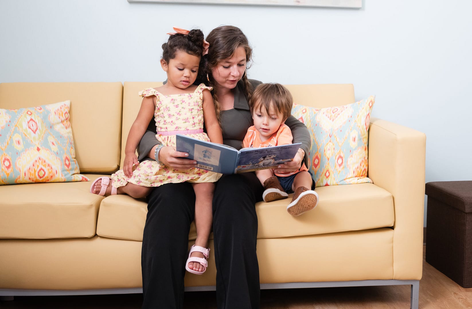 Woman reading to children on yellow sofa.