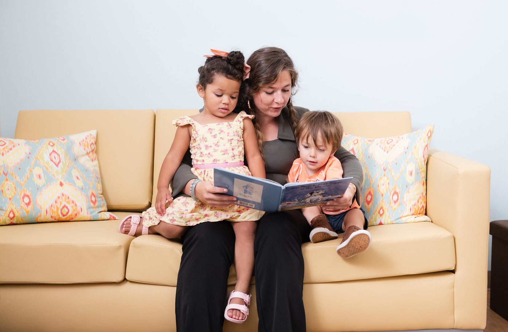 Woman reading book to two children on sofa.