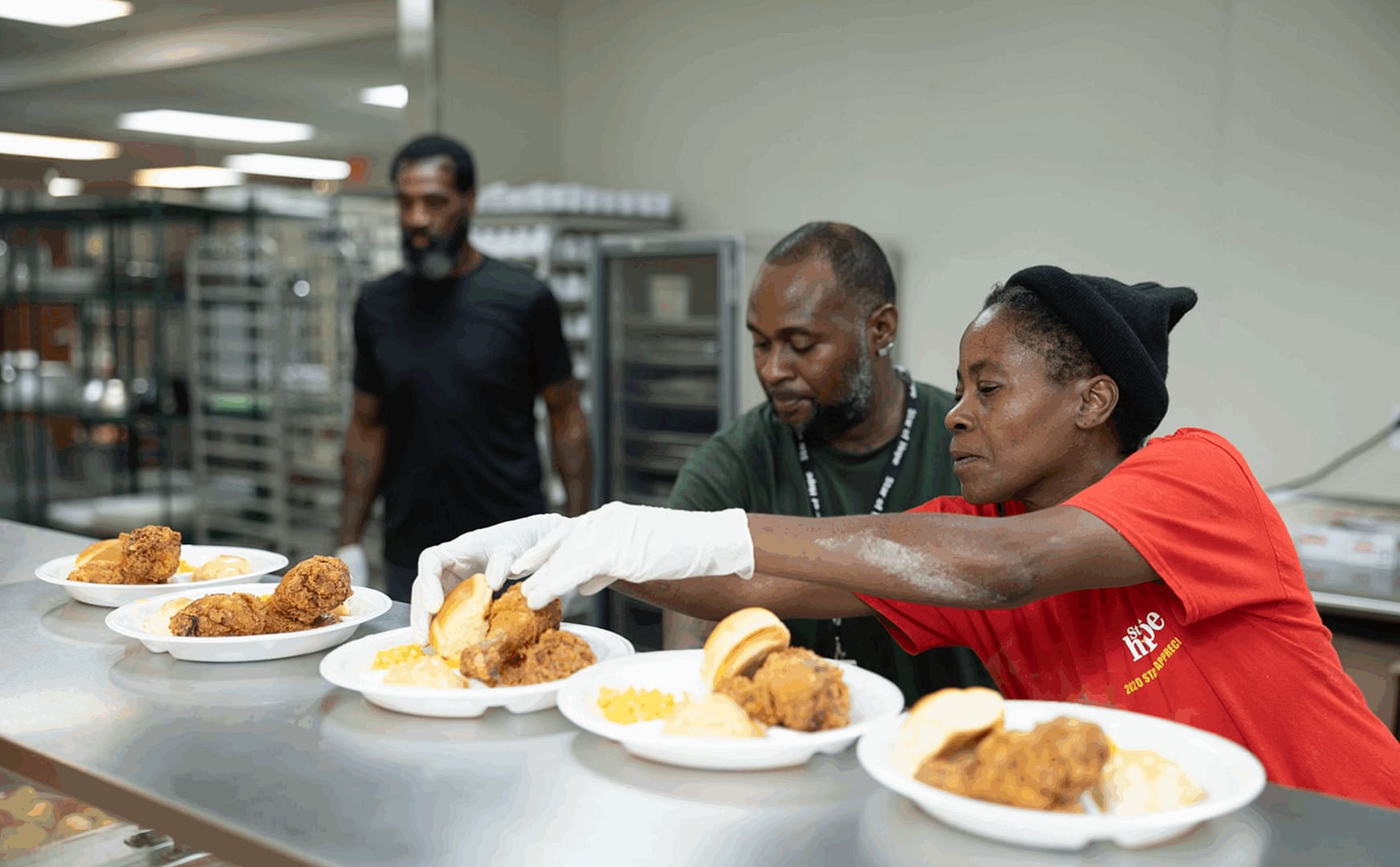 Volunteers serving fried chicken meals in kitchen.