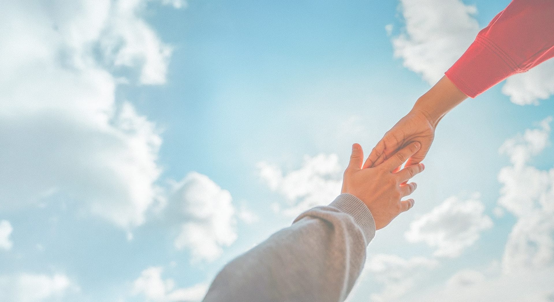 Two hands reaching against blue sky.