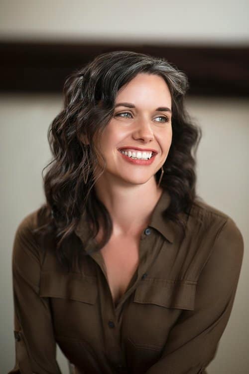 Smiling woman with wavy brown hair, wearing brown shirt.