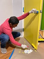 Person painting door with yellow paint in progress.