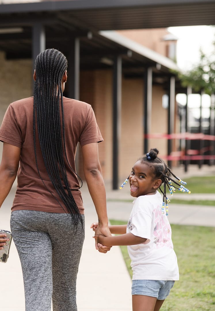 Woman holding hands with two children, walking outside.