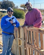 Two men assembling wooden pallets outdoors.