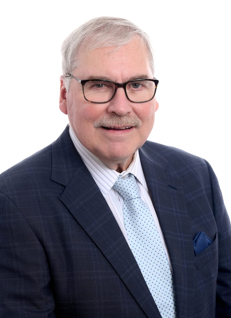 Elderly man in glasses and suit smiling.