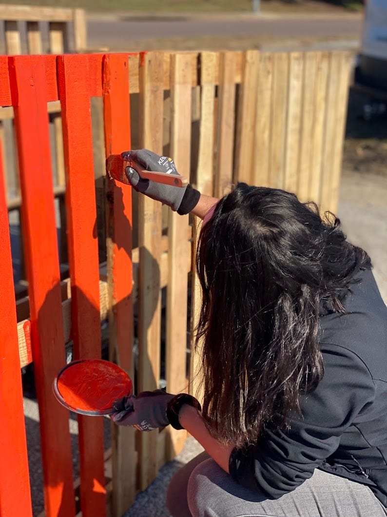 Person painting wooden fence orange outdoors.