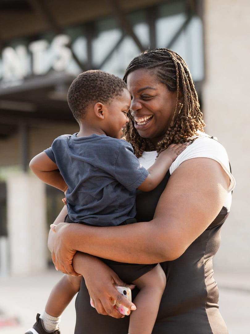 Smiling woman holding a young child outside.