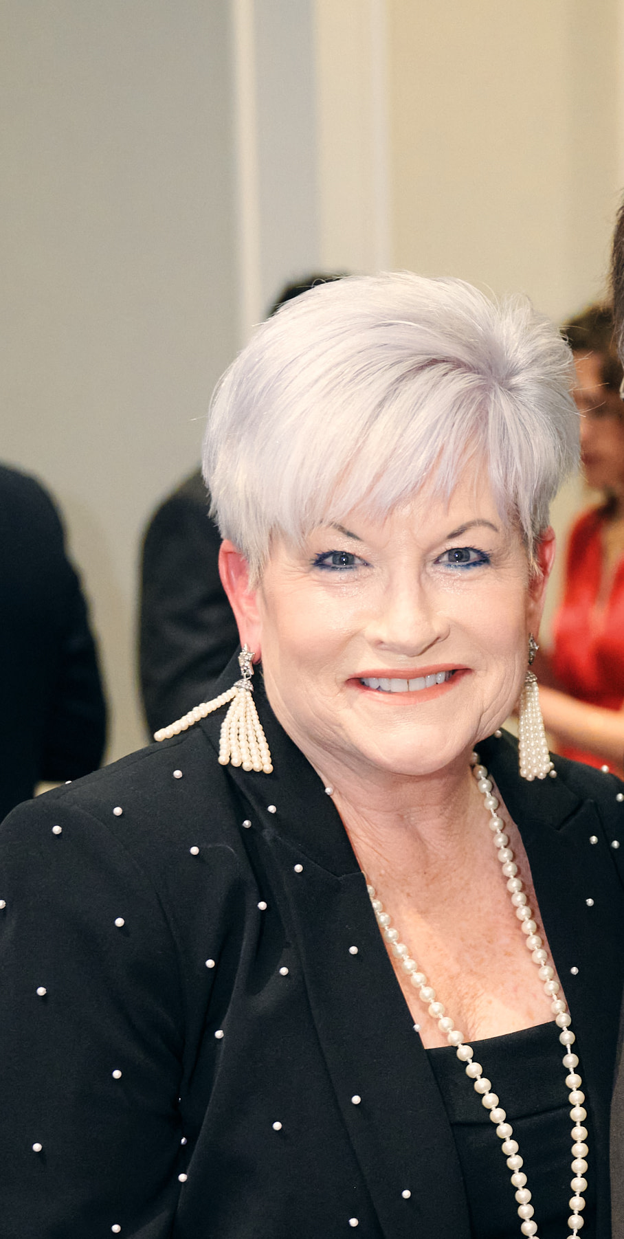 Smiling woman with white hair and pearl jewelry.